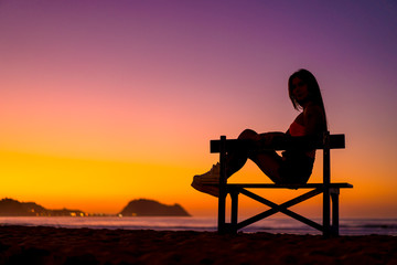 Lifestyle, beautiful silhouette of a brunette in a chair on the beach on a sunset looking at the sea