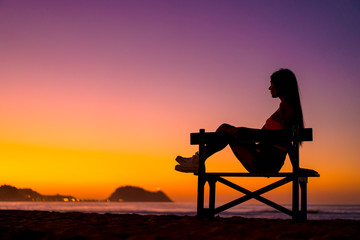 Fototapeta na wymiar Lifestyle, beautiful silhouette of a brunette in a chair on the beach at a sunset