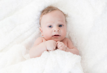 four-month-old white boy with blue eyes lies on a white blanket and take cover with him