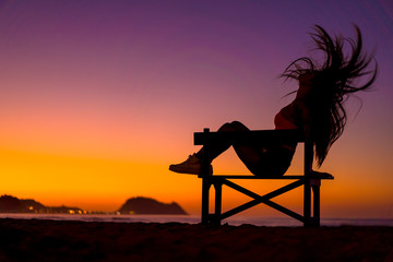 Naklejka premium Lifestyle, silhouette of a brunette in a chair on the beach at night on a sunset