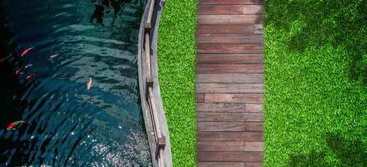 Outdoor Design Concept : Top view of fresh water in pond with green grass meadow field with wooden walkway in outdoor garden.