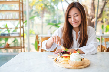 A beautiful asian woman eating a mixed berries pancakes with ice cream and whipped cream by wooden spoon