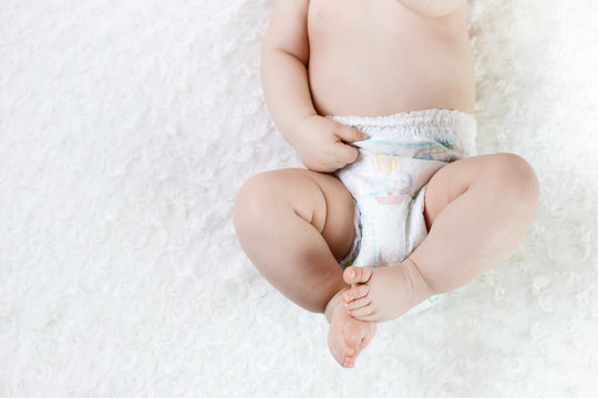 feet of a six months old baby wearing diapers lying on the bed