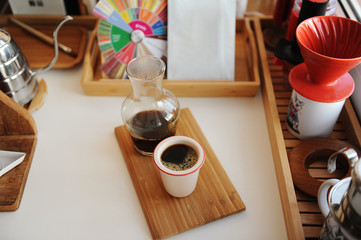 Black filter coffee is served in glass decanter with cup on wooden tray. Manual brewing third wave still life.