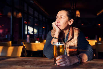 Unhappy, depressed and lonely middle age woman sitting at the bar with a beer glass