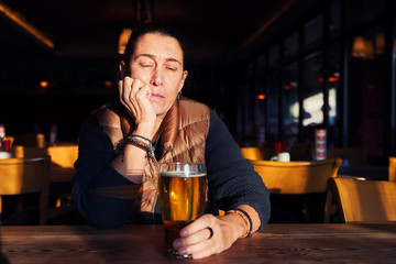 Unhappy, depressed and lonely middle age woman sitting at the bar with a beer glass