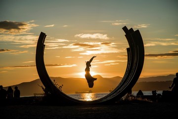 Sunset silhouette happy female jumping inside structure during beautiful sunset in pacific north west Canada on beach English bay Vancouver Friday happiness 