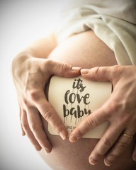 Pregnant woman holding her hands with love and sign saying its love baby during late pregnancy with large belly 