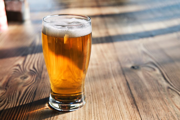 Glass of cold beer on the wooden table of a pub under natural afternoon light