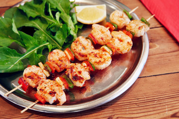 Grilled shrimp skewers in a plate served with garden rocket and lemon