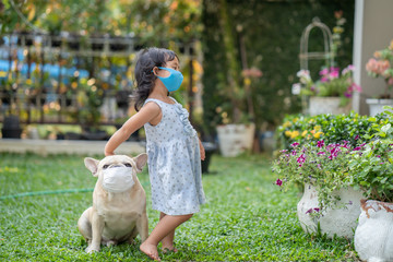 Little girl and her french bulldog standing in garden wearing medical mask prevent pollution, flu and convid-19.