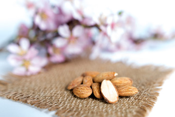 Close up of healthy raw almonds placed on a rustic woven brown mat, with floral decoration blurred in the background