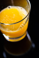 Orange juice on a transparent glass isolated on a black background close up still