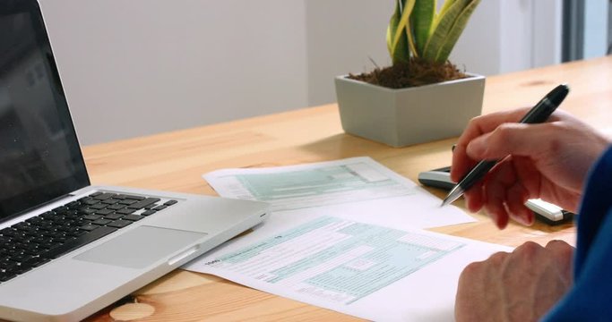 Over the shoulder closeup of man calculating and filling US tax form 1040 by hand and pen with calculator and laptop in the office. 4k footage resolution.