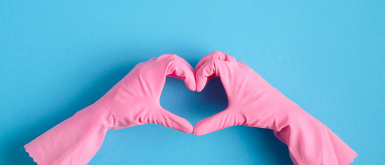 Heart shaped hands in pink rubber gloves over blue background. House cleaning service and housekeeping concept - obrazy, fototapety, plakaty