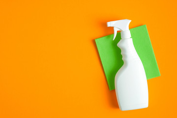 Blank cleaning spray bottle and green rag on orange background. Flat lay, top view. House cleaning...