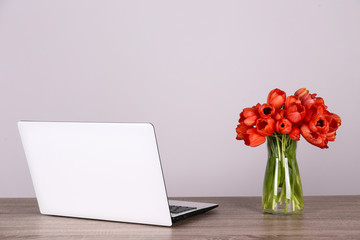 Fresh flower composition, bouquet of darwin hybrid tulips with black and white laptop computer, white wall background. Office romance concept. Copy space, close up, top view, flat lay.