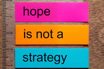 Three bookmark stickers with the words hope is not a strategy on a dark natural wooden table