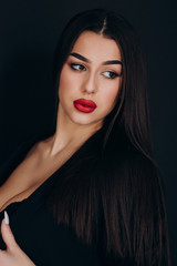 a young girl with dark hair, brown eyes and bright red lips poses in a Studio in a black pantsuit