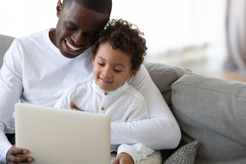 Fototapeta premium Loving African American father teaching little son to use laptop