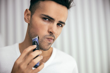 Young guy trimming his beard with trimmer