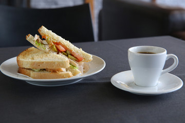 Cup of coffee and a sandwich with lettuce on a table