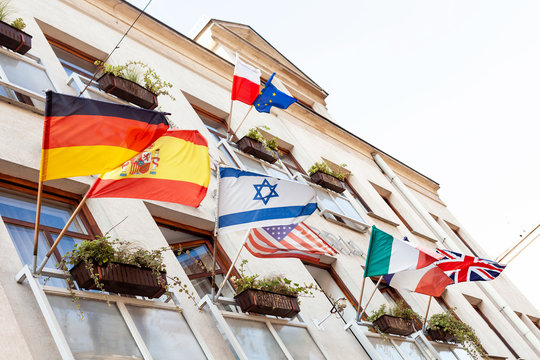 Multiple waving flags on a building facade in the wind, Israel, Germany, Spain, USA, Poland, European Union, Italy, France, UK, many nations, multinationality, global citizenship abstract concept