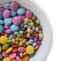 Chocolate candies with coloful glazes in a white bowl isolated on white background
