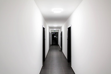 Simple clean newly built generic modern new real estate block of flats interior, long white corridor with black doors, perspective. New bought apartment, new home, hallway abstract concept, copy space
