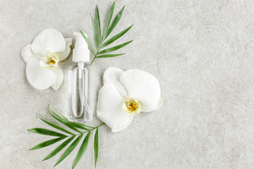 Obraz na płótnie Canvas Bottle with hyaluronic acid / essential oil, tropic palm leaves on gray marble background. Concept of modern beauty. Natural / Organic cosmetics products. Flat lay, top view.