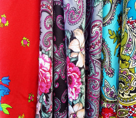 Multiple colorful pieces of traditional simple Polish flowery fabric with floral themes patterns. Multi colored cloth hanging at a market stall macro, closeup. Abstract background, vibrant texture.
