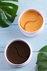 Two plastic containers of collagen patches for eye skin care on a light blue wooden background.