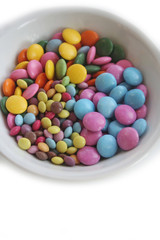 Chocolate candies with coloful glazes in a white bowl isolated on white background