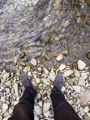 Traveller in dirty trousers and shoes standing on the rocks, rocky seaside / riverside, scene near a river First person pov muddy trekking shoes resting while travelling abstract concept, destinations