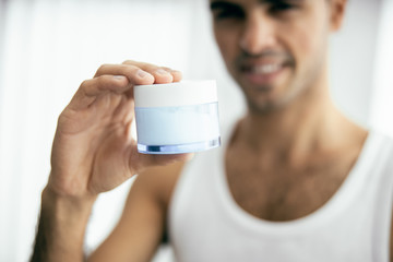 Happy young man showing jar of cream
