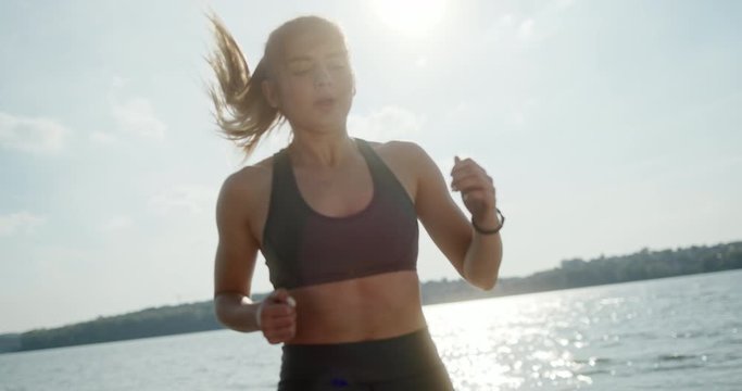 Muscular fit young woman jogging on the spot on a wooden deck overlooking water for a healthy cardiovascular workout to burn calories in a fitness and active lifestyle concept.