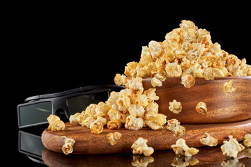 Popcorn flakes in a wooden bowl and 3D glasses isolated on a black background.