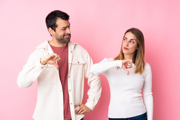 Couple in Valentine Day over isolated pink background showing thumb down sign with negative expression