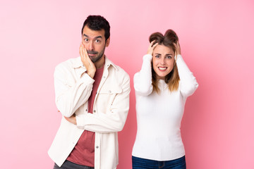 Couple in Valentine Day over isolated pink background takes hands on head because has migraine