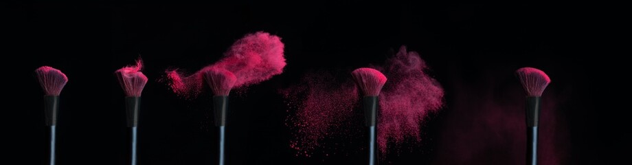 Five make-up brushes with sequence of pink powder explosions on black background