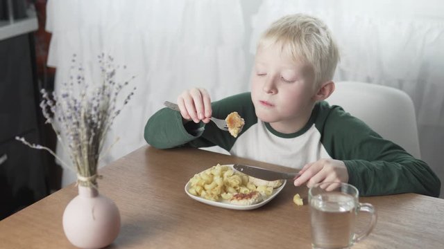 The blond boy dines at home with pasta and meatballs.