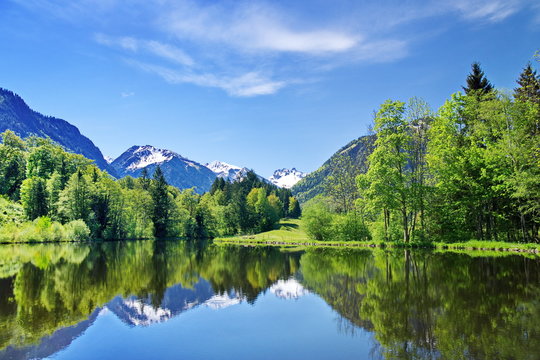 Bergsee im Fr&uuml;hling in den Alpen mit Gipfel und Schnee