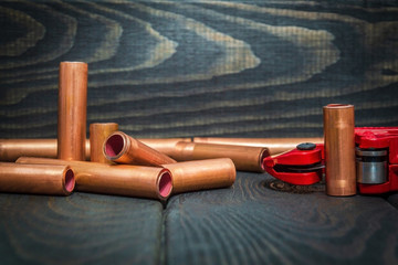 Red pipe cutter and copper pipes with connectors for plumbing repairs on black boards