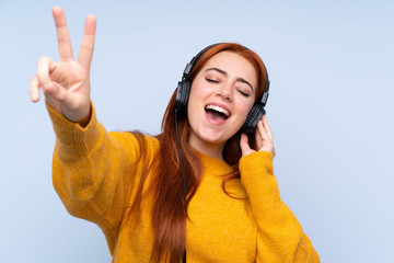 Redhead teenager girl over isolated blue background listening music and singing