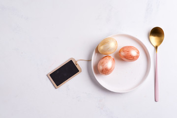 Obraz na płótnie Canvas Greeting card with handmade painted bright eggs on a plate and golden spoon on a light grey marble background.