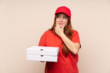 Pizza delivery teenager girl holding a pizza over isolated background thinking an idea