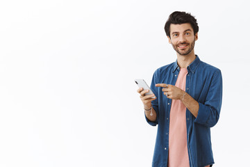 Handsome bearded man talking to you and pointing smartphone display as smiling and telling own...