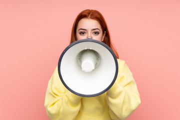 Redhead teenager girl over isolated pink background shouting through a megaphone