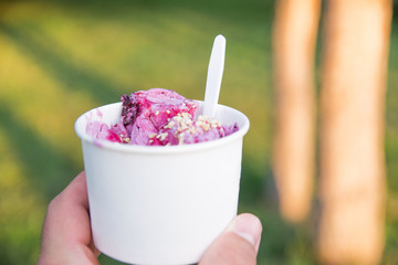 Cup of appetizing ice cream with peanuts in male hand on the background of green grass in park.