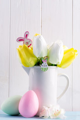Congratulation Easter card with fresh tulips, handmade painted eggs and decotation against light grey wooden background.